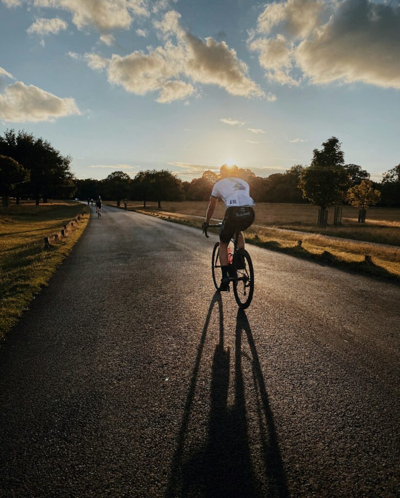 A cyclist riding away down a park road at sunset